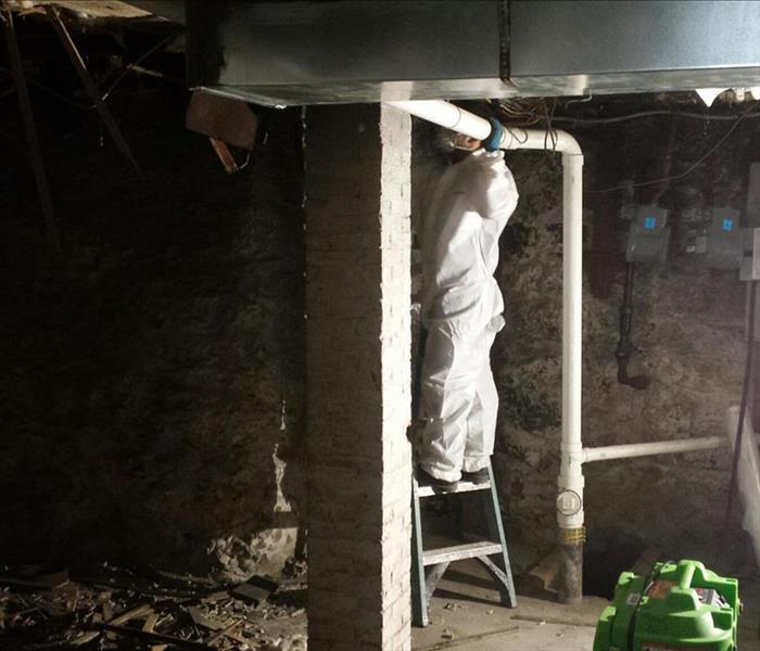 SERVPRO tech cleaning the soot covered walls of a basement.