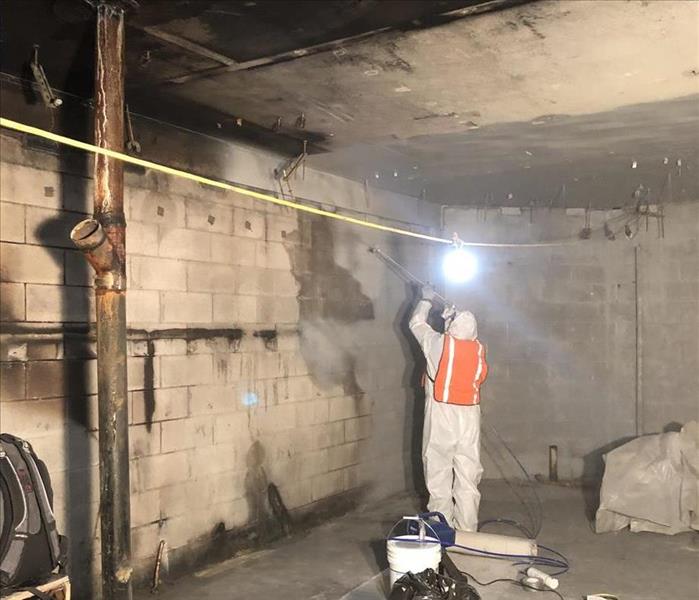 A SERVPRO tech gets ready to clean the walls of a basement covered in soot.