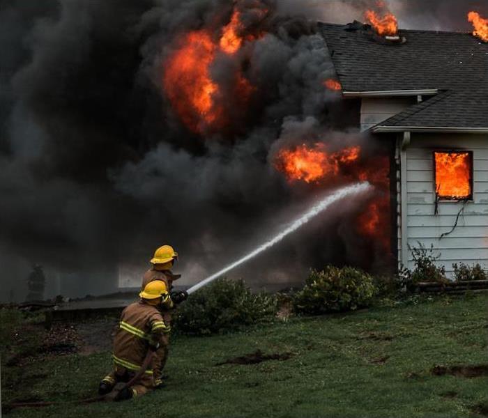 Two firefighters actively fighting a house fire using a powerful hose