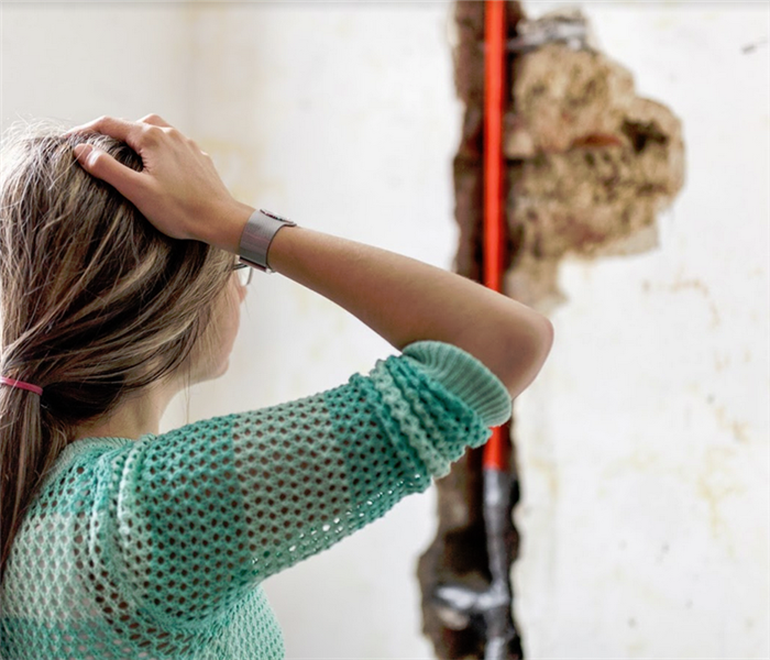 woman looking at water damage in a pipe in a wall